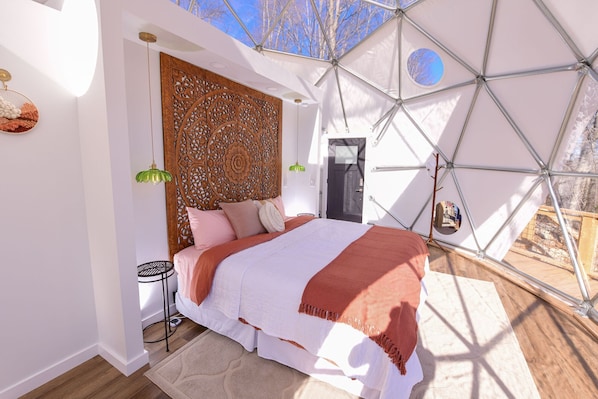 Un dormitorio con una estructura de techo geométrica, un cabecero de madera y una cama con colcha blanca y naranja.