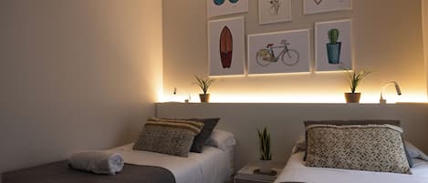 A hotel room with two beds, a nightstand, and wall art including sunglasses, a surfboard, a bicycle, and a cactus.