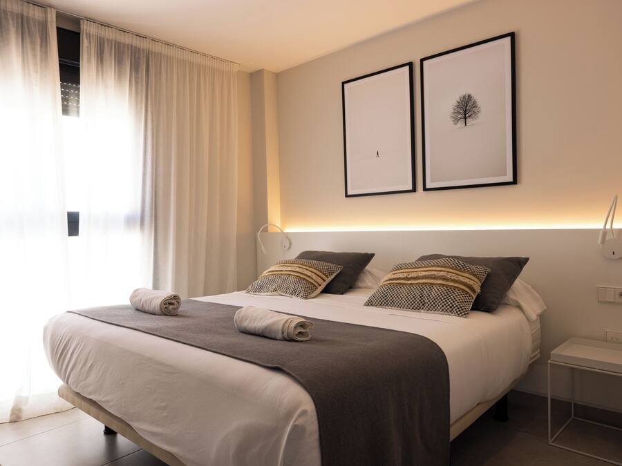 Ein ordentlich bezogenes Bett mit einer braunen und weißen Tagesdecke, zwei gerahmte Bilder an der Wand und ein Nachttisch mit einer Lampe.