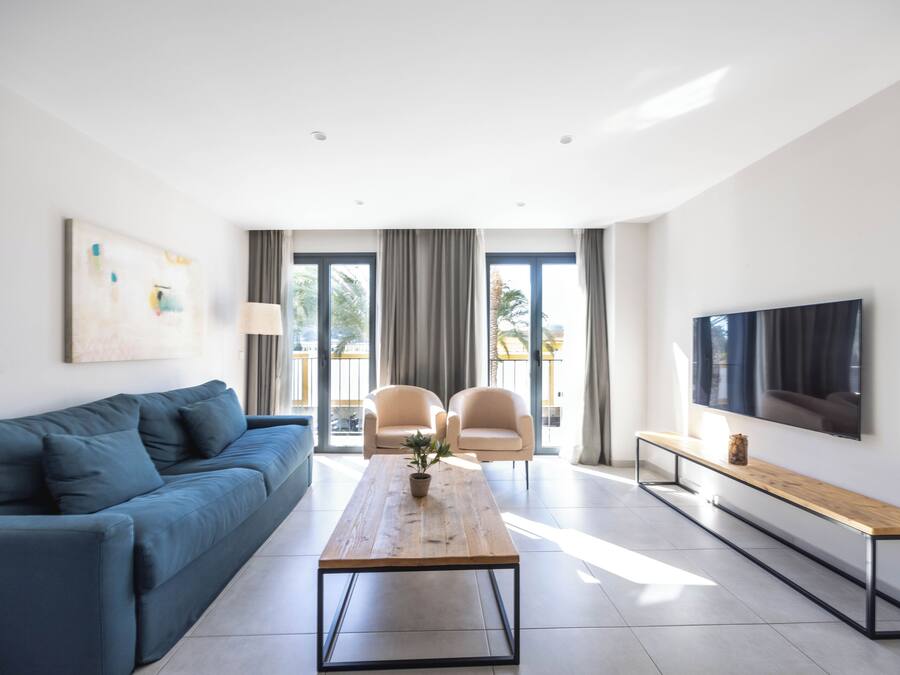 Una sala moderna con un sofá, dos sillones, una mesa de centro, un televisor y un balcón con cortinas.
