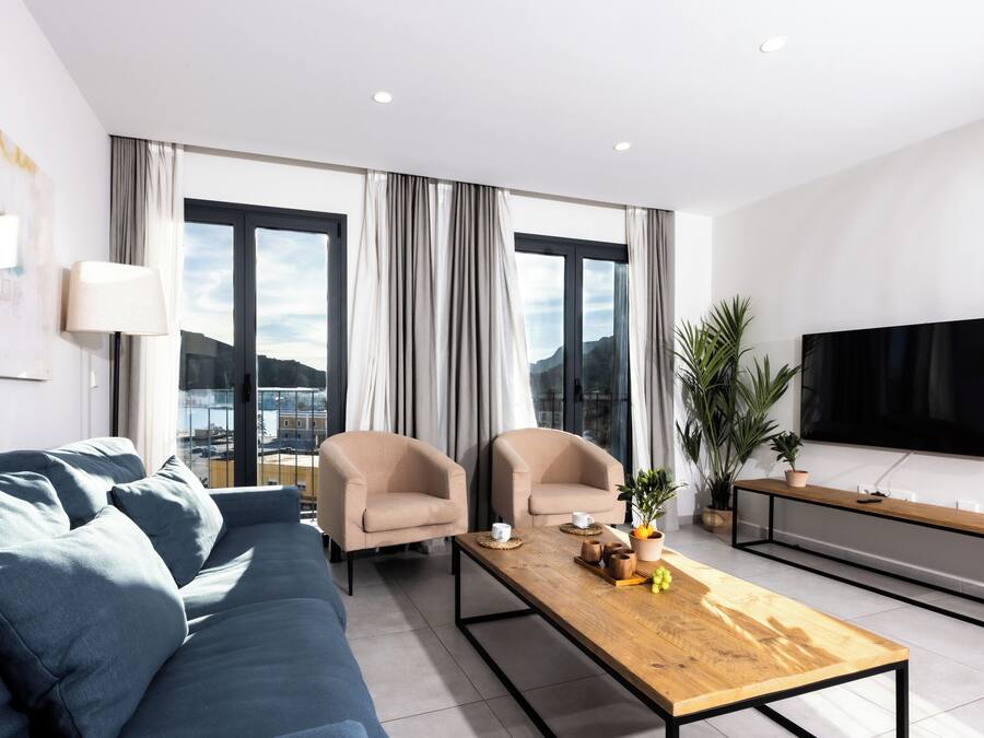 Un salon moderne comprenant un canapé, deux fauteuils, une table basse en bois, un téléviseur et une grande fenêtre avec des rideaux.