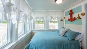 Une chambre à coucher avec un lit, des rideaux, une vue sur l’extérieur et un luminaire fixé au mur.