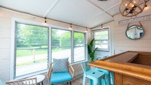 Une pièce chaleureuse avec un bar en bois, des chaises en osier et une grande fenêtre donnant sur l’extérieur.