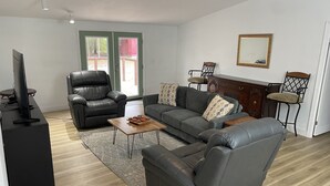 Una sala moderna con un sofá de cuero, un sillón negro, una mesa de centro de madera y un televisor sobre un mueble.