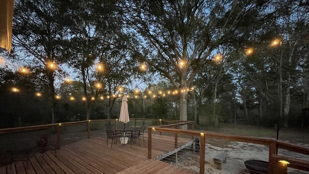 Una terraza de madera con luces colgantes, una mesa con sillas y un área cubierta.
