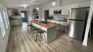 Una cocina moderna con una isla central, taburetes de bar, un refrigerador de acero inoxidable y muebles de cocina blancos.