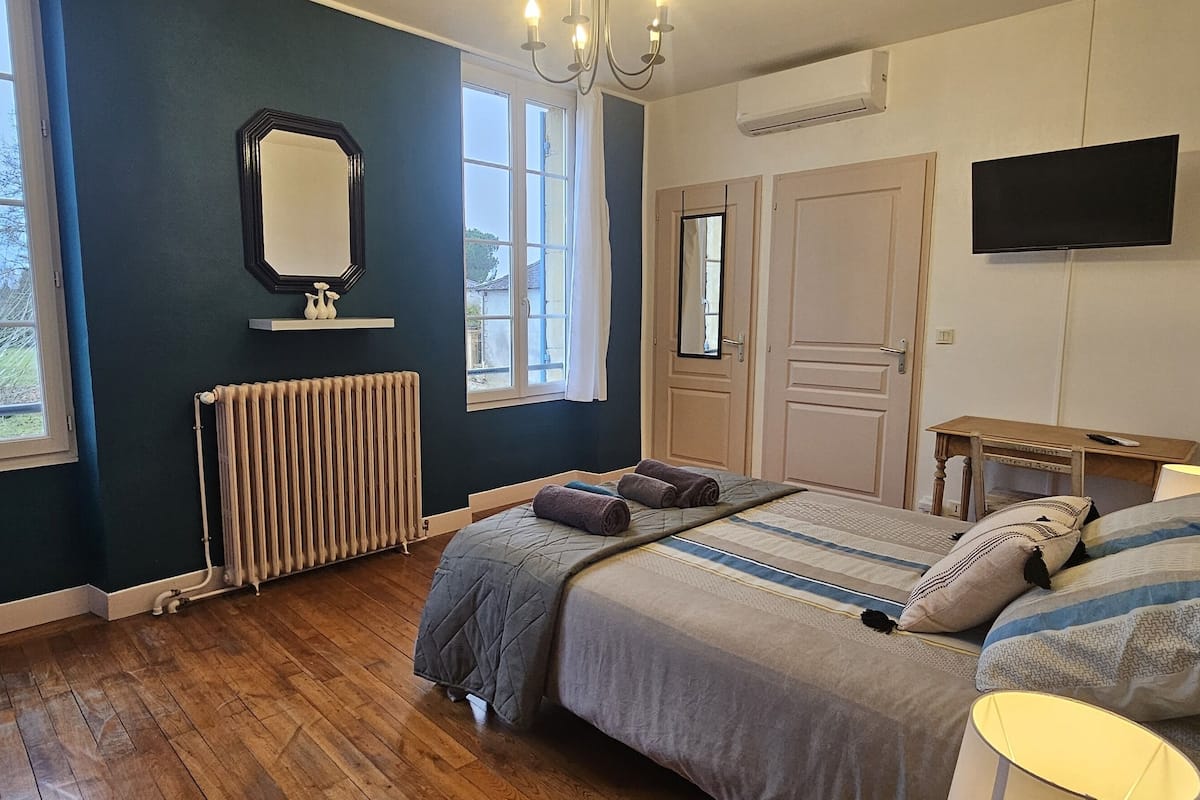 A bedroom with a large bed, a television, a radiator, and a window with curtains.
