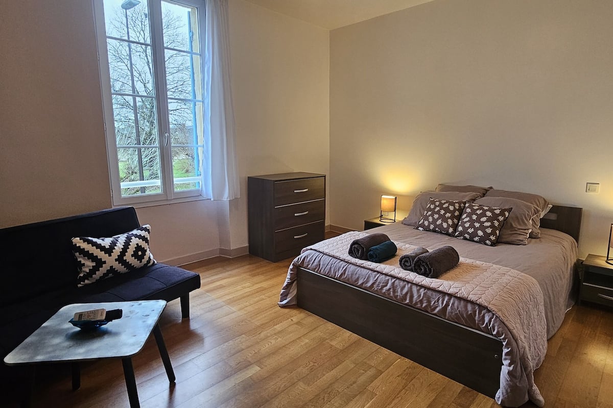A bedroom with a bed, bedside tables, a nightstand, a dresser, a sofa, and a window.