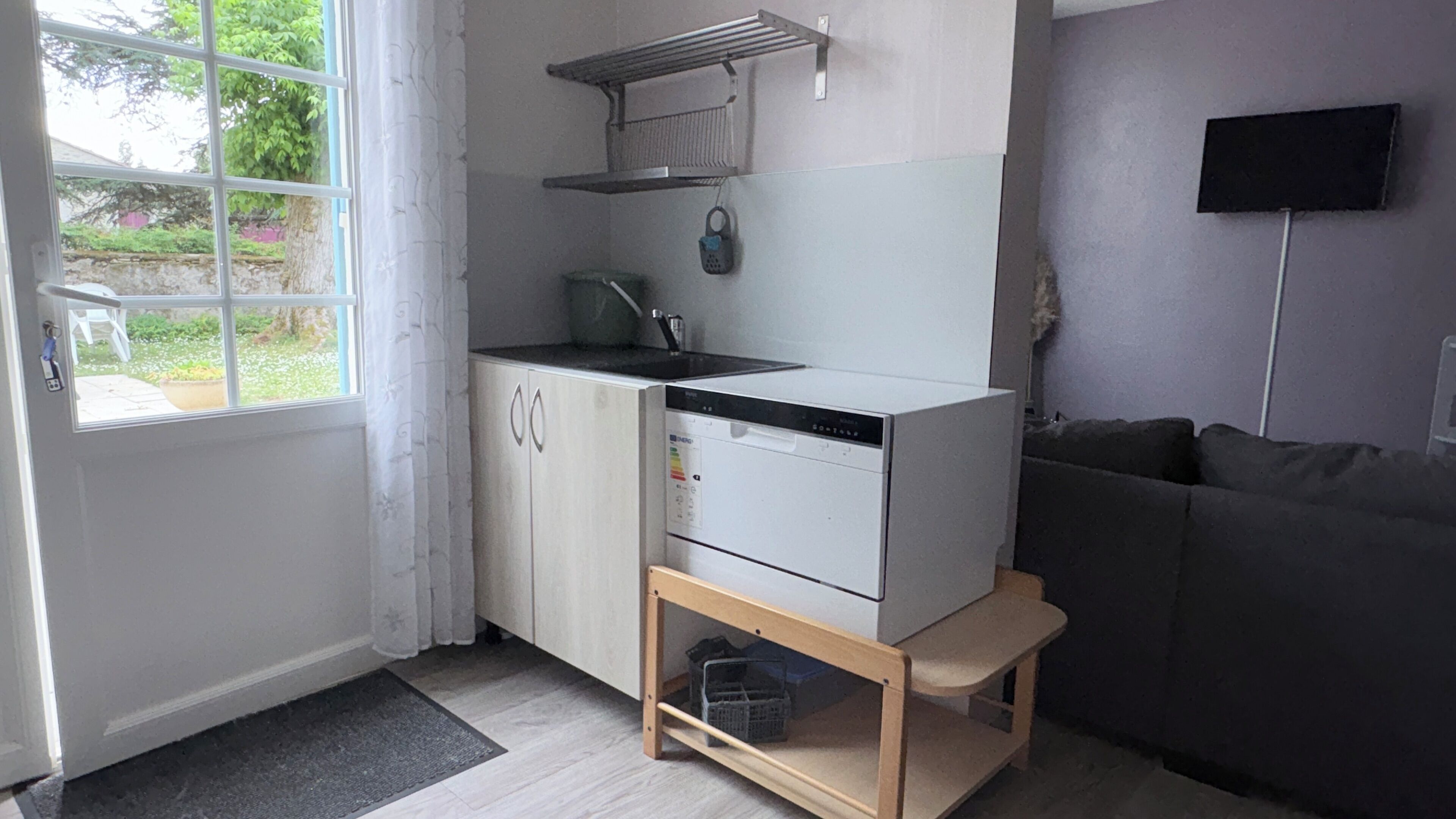 A compact kitchen with a built-in dishwasher, a small countertop, and a window with curtains.