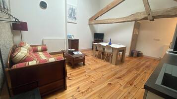 Un salon chaleureux avec un plancher en bois, un canapé, une table à manger avec des chaises, un téléviseur et une cheminée.