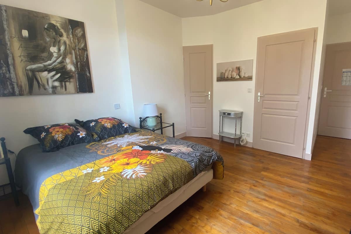A bedroom with a bed, a nightstand, a lamp, a door, and a painting on the wall.