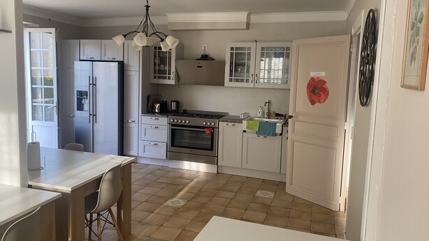 A kitchen with white cabinets, a stove, a sink, and a dining area with a table and chairs. - Les Deux Chênes (Le Fleix)