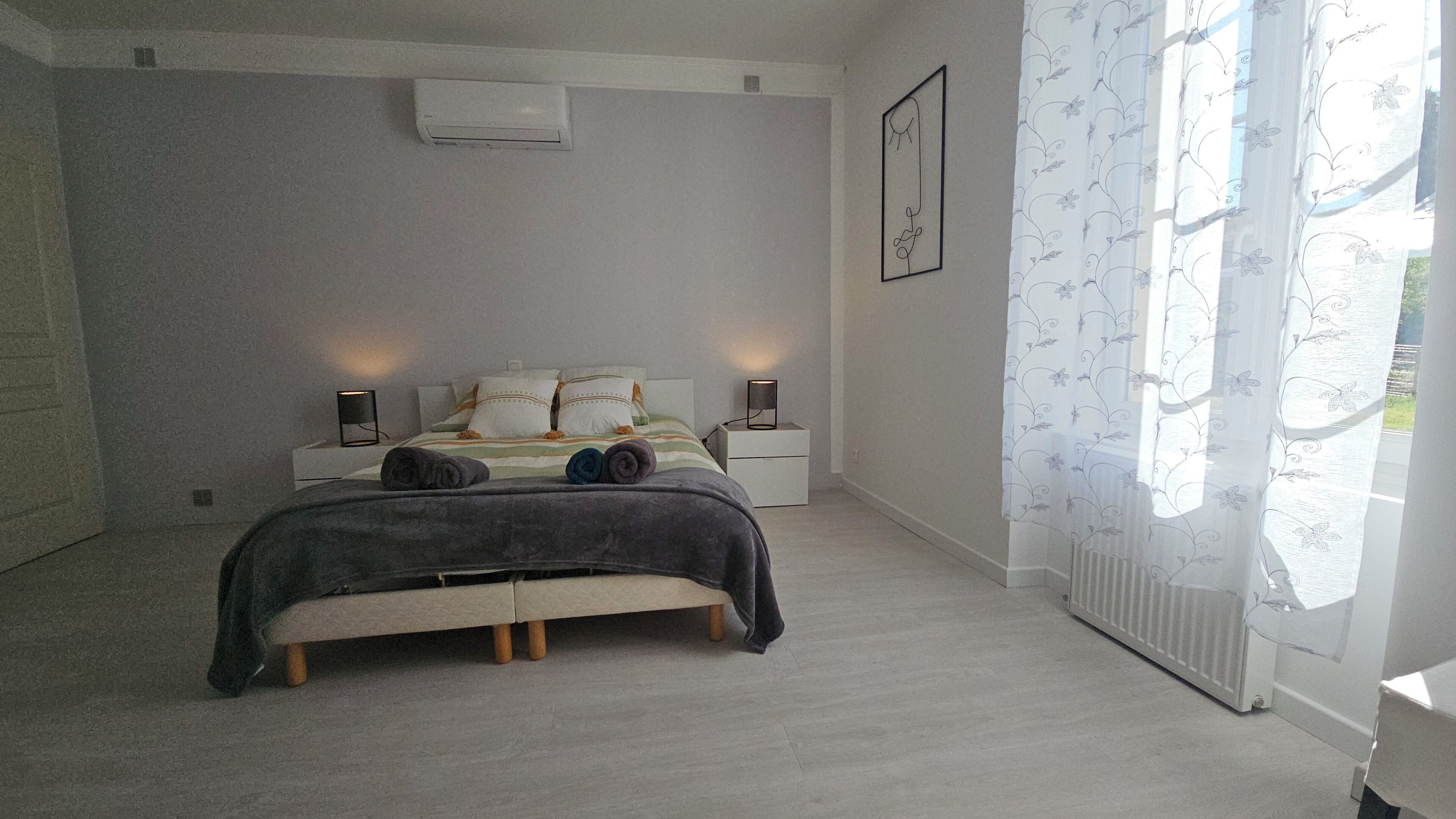 Quarto com cama, mesas de cabeceira, radiador e janela com cortinas.