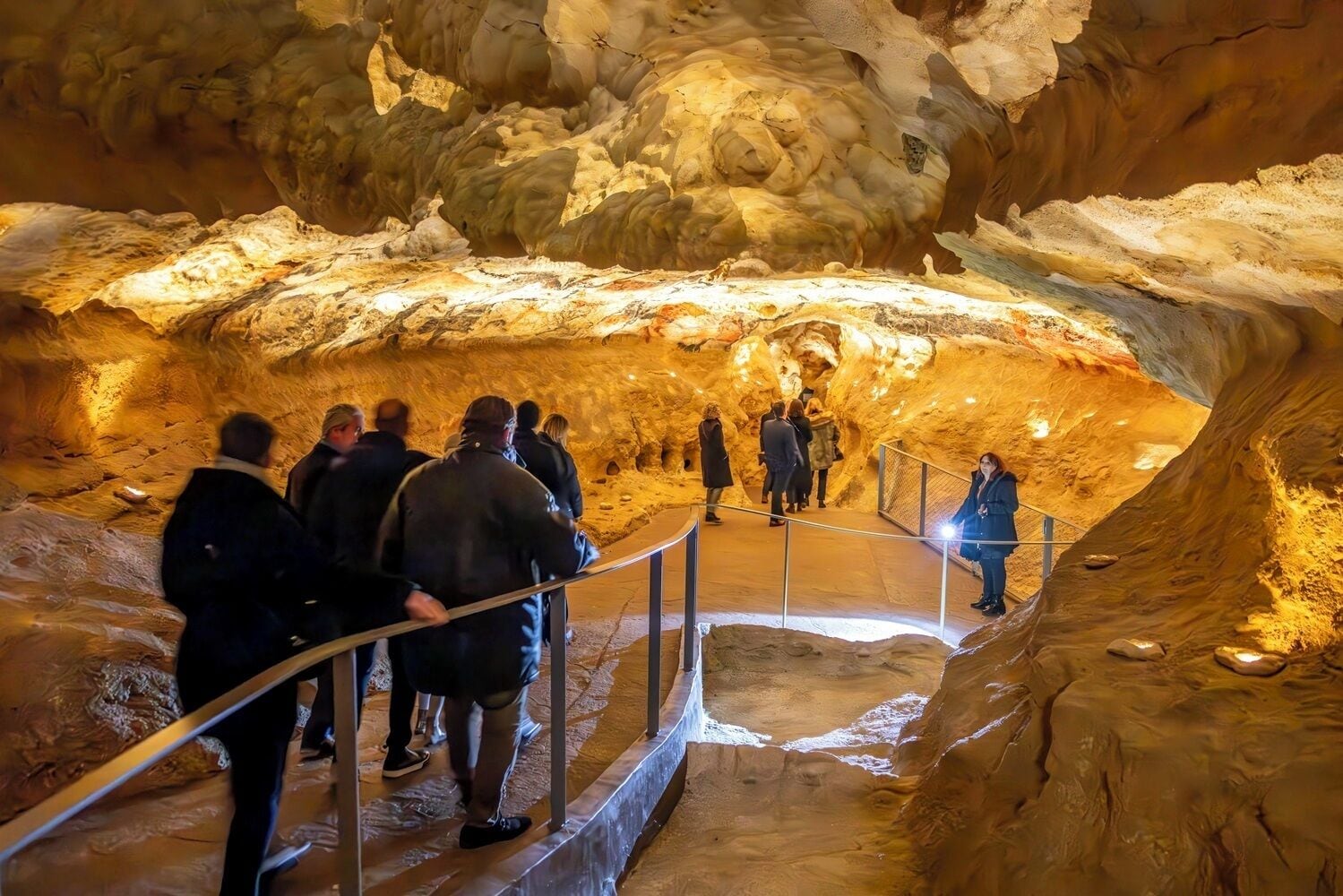 Visitas turísticas exploram uma gruta por meio de uma passarela metálica.
