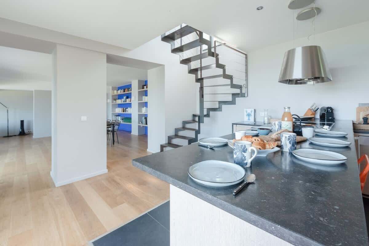 Een moderne keuken met een bijzondere spiraaltrap, een eethoek met borden en bestek, en een boekenkast op de achtergrond.