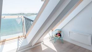 Una habitación con techos altos, tragaluces, vista al mar, una alfombra mullida y un sillón.