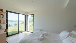 Un dormitorio moderno con una cama grande, un escritorio y vistas a un lago a través de un ventanal corredera.