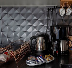 A kitchen with a black countertop, a coffee maker, a kettle, a wire rack, and packaged snacks. - Ibira Oásis - Imbituba - SC (Imbituba)
