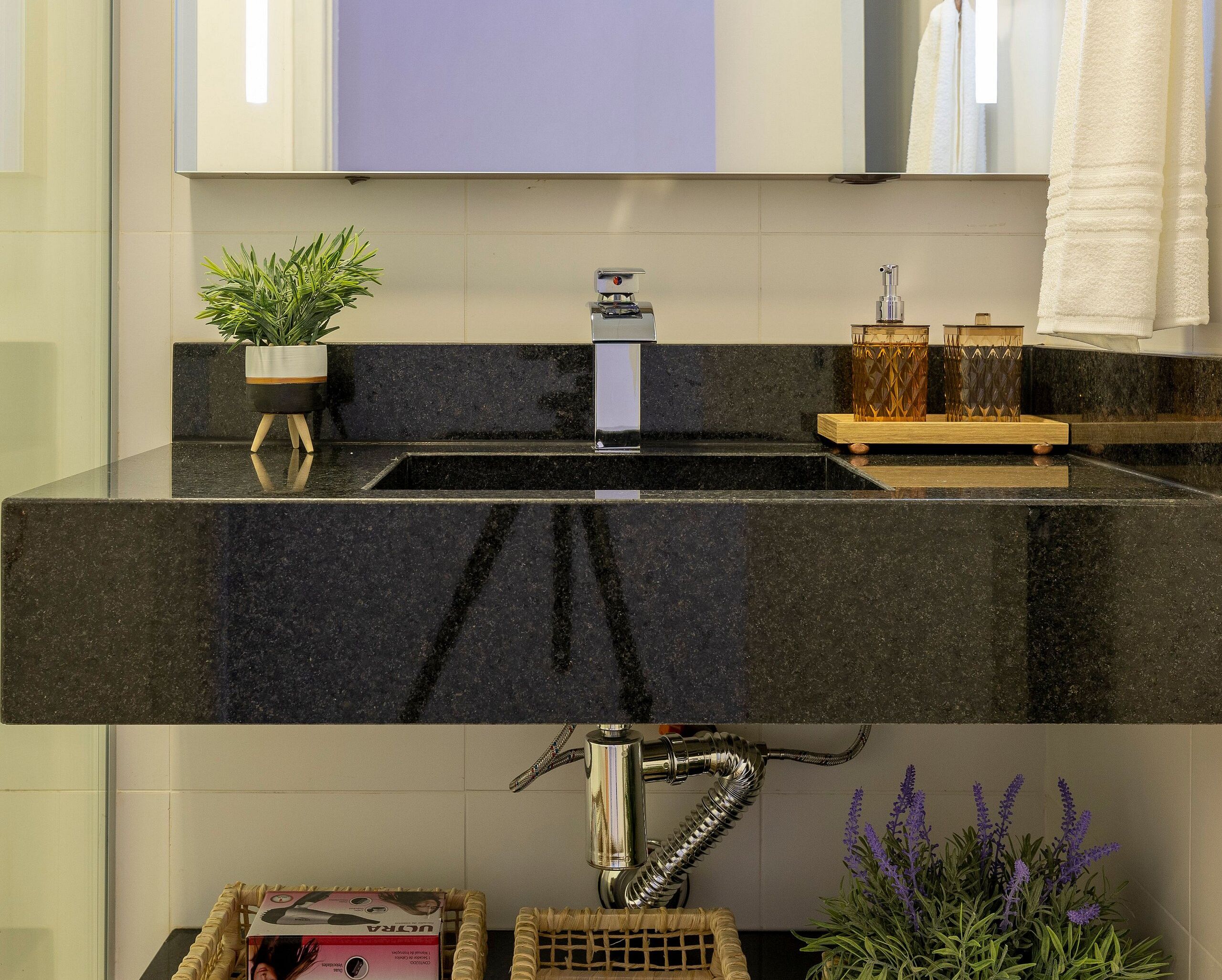 Un baño con lavamanos de mármol negro, un espejo, una planta en maceta y una botella de jabón líquido.