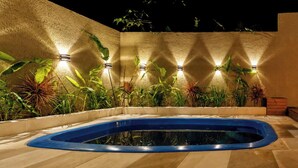 A swimming pool with a blue interior, surrounded by plants and walls with embedded lights. - Ibira Oásis - Imbituba - SC (Imbituba)