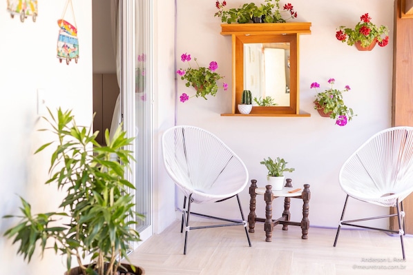 A room with two white wireframe chairs, a small wooden table, and a mirror on the wall. - Ibira Oásis - Imbituba - SC (Imbituba)