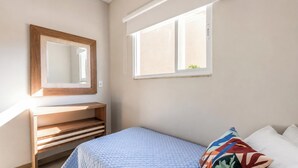 A bedroom with a bed, a bedside table, a mirror, and a window. - Ibira Oásis - Imbituba - SC (Imbituba)