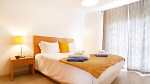 A hotel room with a bed, two bedside lamps, a nightstand, and a window with curtains.