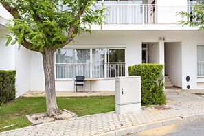 A modern building with a balcony, a small garden area with a tree, and a compact refrigerator on the sidewalk.