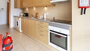 A kitchen with wooden cabinets, a washing machine, a stove, and a fire extinguisher.