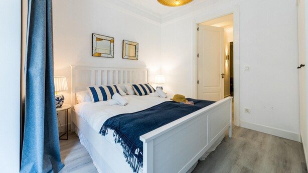 Une chambre à coucher bien rangée, avec un lit, des lampes de chevet, un miroir et une porte donnant sur une autre pièce.