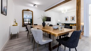 Un coin repas avec une table en bois, des chaises blanches et noires, un grand miroir et une plante en pot.