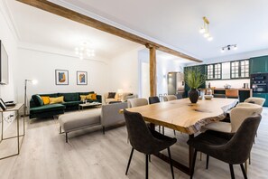 Een moderne woonkamer met een houten eettafel, banken en een keuken op de achtergrond.