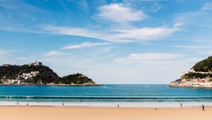 Une plage avec un ciel dégagé, une eau calme et des bâtiments situés sur les flancs des collines.