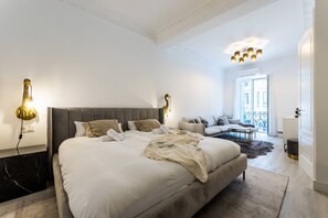 A modern bedroom with a large bed, a sofa, and a dining area.
