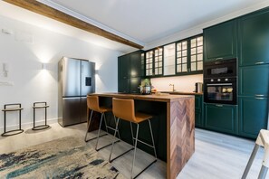 A modern kitchen with a central island, bar stools, a built-in oven, and dark green cabinets. - BALEA SUITE APARTMENT (San Sebastián)
