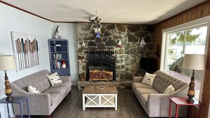 A cozy living room with two sofas, a stone fireplace, a bookshelf, and a wooden coffee table. - Charming Lakefront Cabin on Mason Lake with Pebble Beach and Private Dock (Grapeview)