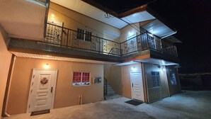 Un immeuble de deux étages doté d’un balcon à l’étage supérieur, d’une porte ornée d’une guirlande et d’une entrée fermée par un portail.