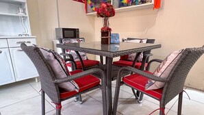 Un coin repas avec une table en verre entourée de chaises en osier dotées de coussins rouges.