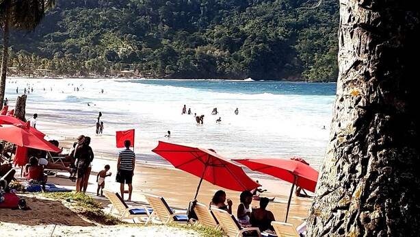 Une plage où l’on peut se baigner et bronzer, avec des parasols rouges et une falaise rocheuse.