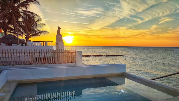 Ein Pool mit Blick auf den Sonnenuntergang über dem Meer, eine Statue und eine Ziegelmauer.