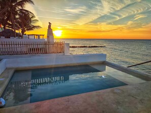 Una piscina con vista al atardecer sobre el mar, una estatua y una valla.