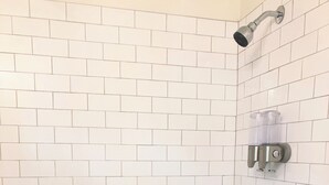 Ein Badezimmer mit weißen Fliesen im U-Bahn-Stil, einer Duschbrause, einer Toilette und einem Waschbecken.