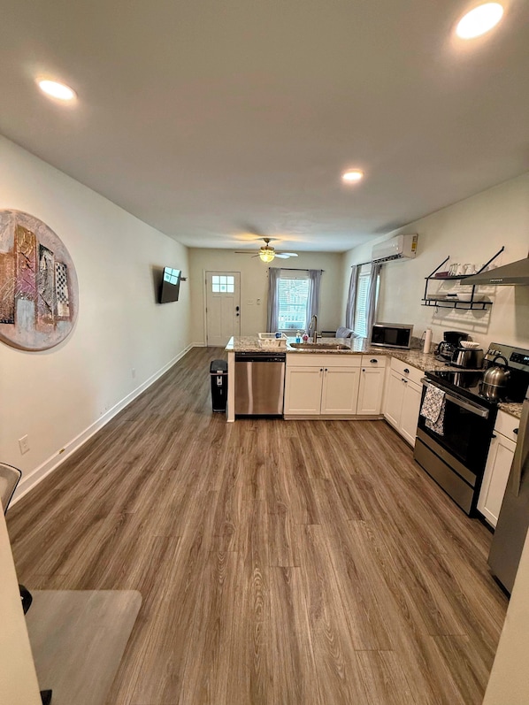 A modern kitchen with wooden flooring, a dishwasher, a stove, and a ceiling fan.