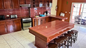 A kitchen with wooden cabinets, a stove, a sink, and a large island with stools.
