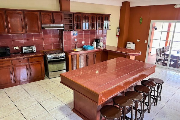 A kitchen with wooden cabinets, a stove, a sink, and a large island with stools. - Rancho Chanel (Santa Ana)