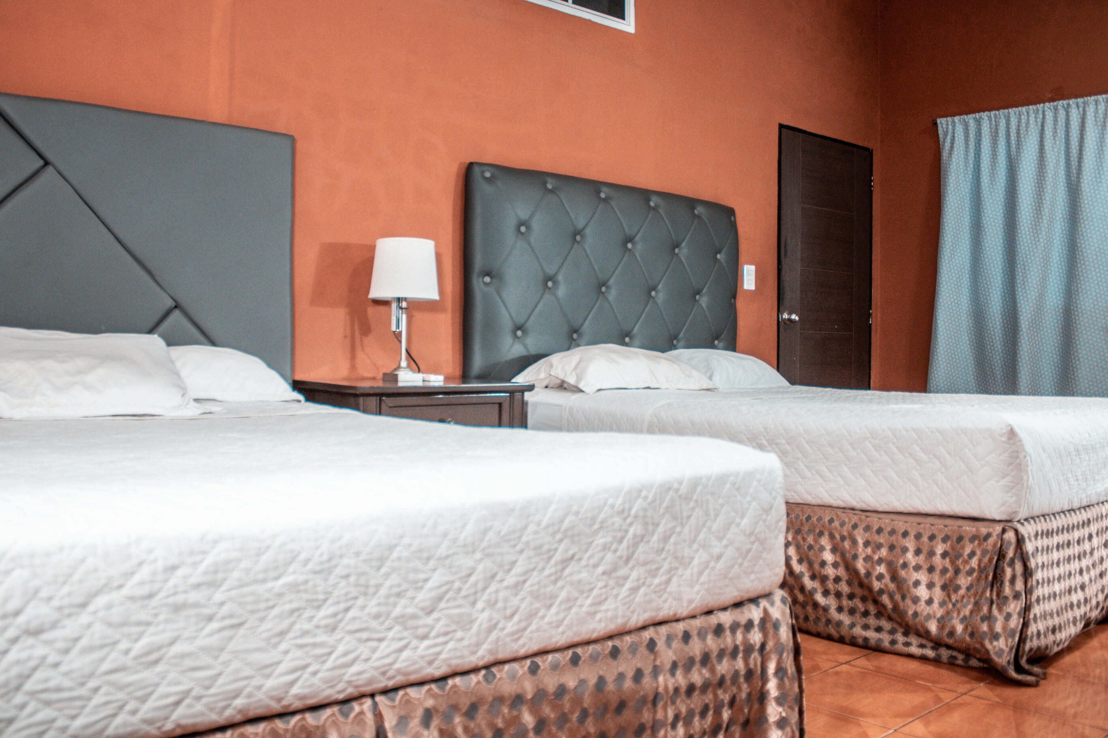 Habitación de hotel con dos camas, una mesita de noche, una lámpara y una puerta.