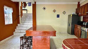 A kitchen with a central island, stools, a refrigerator, and a microwave. - Rancho Chanel (Santa Ana)