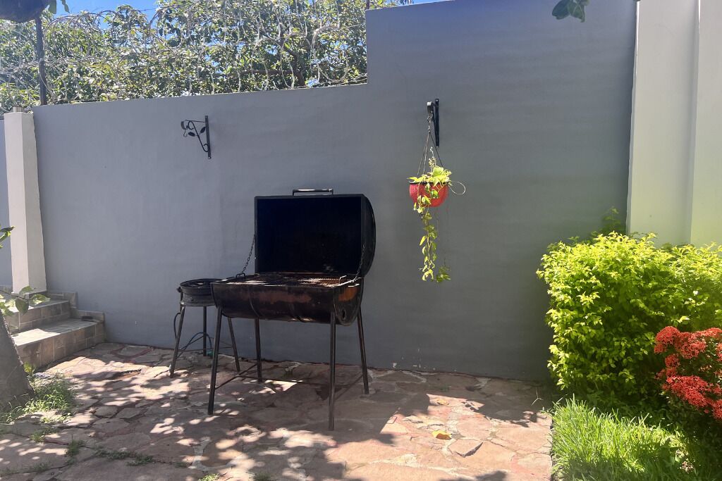 Een barbecue in een terrasgedeelte met een stenen vloer, een grijze muur en een hangplant.