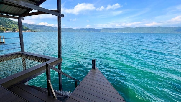 A wooden pier extending into a calm lake with a clear sky above.