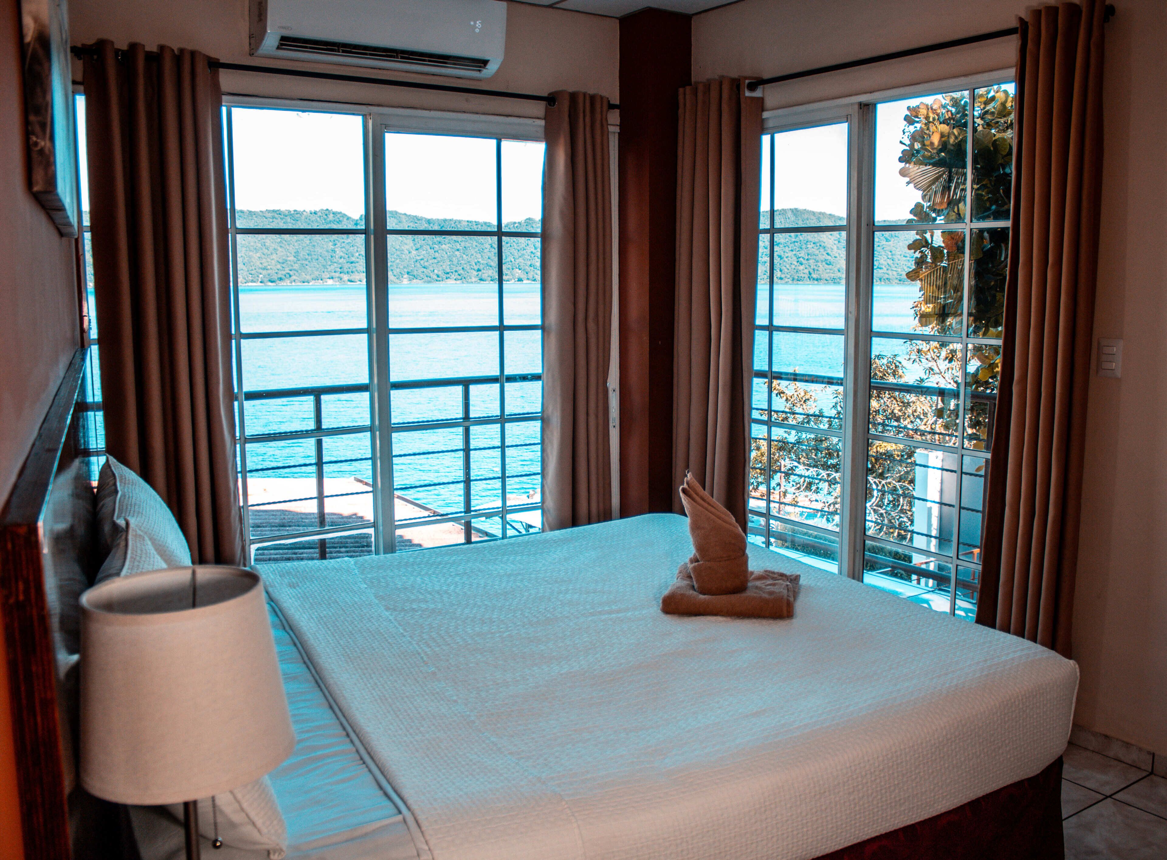A hotel room with a bed, a lamp, and a large window with curtains.
